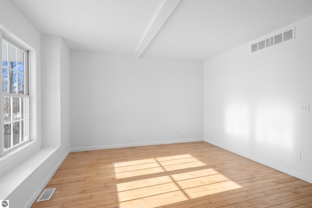 spare room featuring light wood-style flooring, plenty of natural light, and visible vents