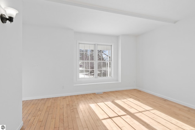 spare room with hardwood / wood-style flooring, beamed ceiling, visible vents, and baseboards