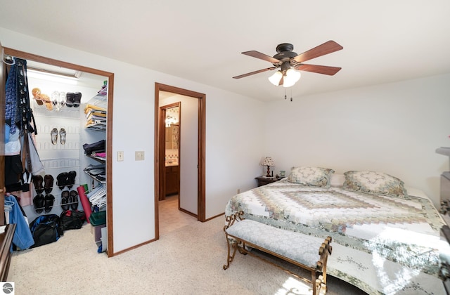 bedroom with a walk in closet, light carpet, a ceiling fan, a closet, and baseboards