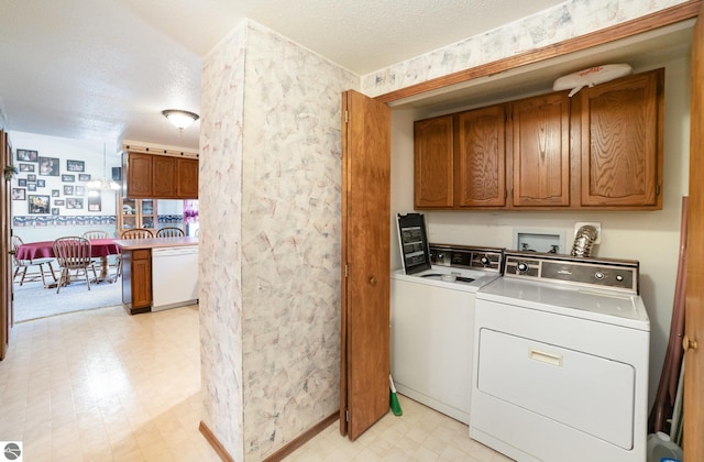 laundry area with a textured ceiling, cabinet space, wallpapered walls, light floors, and washing machine and clothes dryer