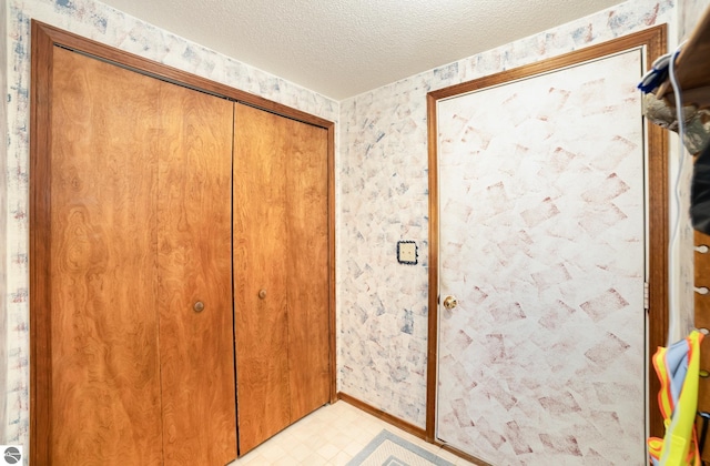 interior space featuring a textured ceiling, light floors, and wallpapered walls