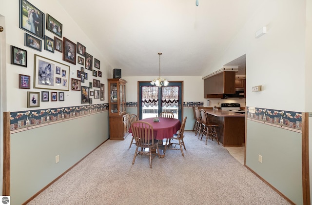 dining area featuring lofted ceiling, wainscoting, a chandelier, and light carpet