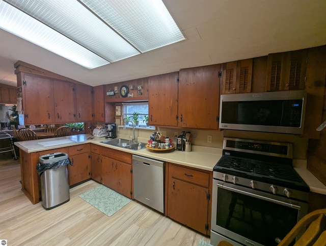 kitchen with light countertops, light wood-type flooring, brown cabinets, appliances with stainless steel finishes, and a sink