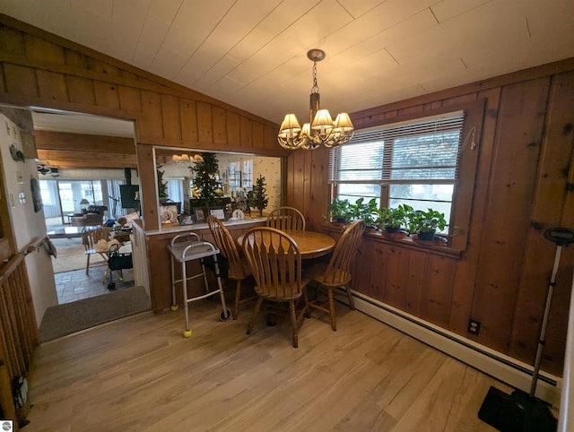 dining room featuring wooden walls, a baseboard radiator, lofted ceiling, light wood-style floors, and a notable chandelier