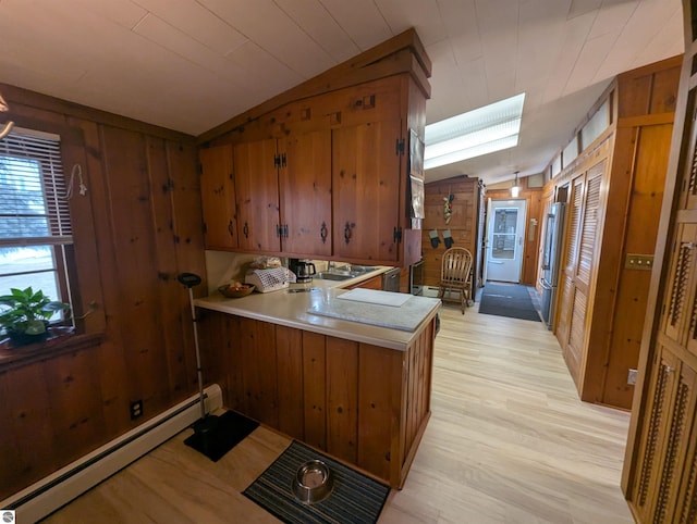 kitchen with a baseboard heating unit, vaulted ceiling, brown cabinets, and wood walls