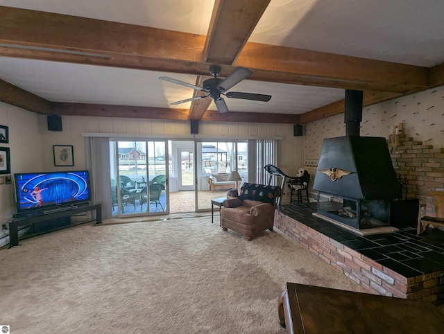 carpeted living area with beamed ceiling, a wood stove, and ceiling fan