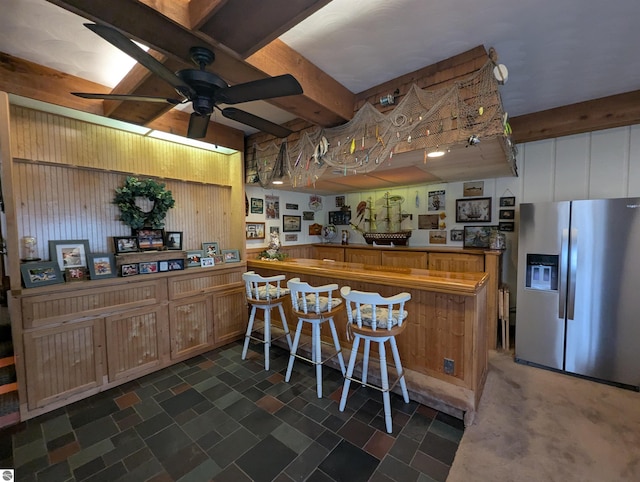 kitchen with a ceiling fan, beam ceiling, stainless steel fridge with ice dispenser, and wood walls