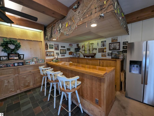 kitchen featuring beam ceiling, stainless steel refrigerator with ice dispenser, and wood walls