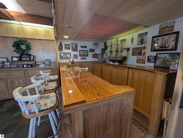 interior space with a wainscoted wall, wooden walls, wood ceiling, and stone finish floor