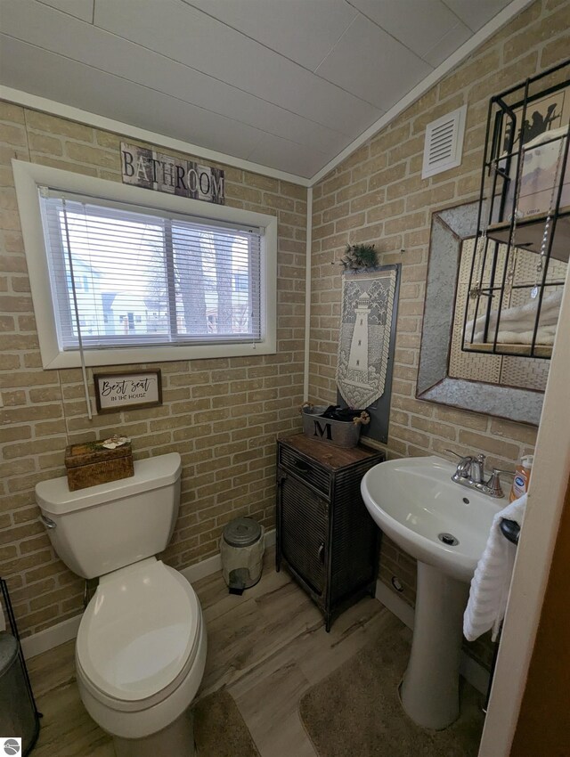 half bath featuring lofted ceiling, wood finished floors, visible vents, and brick wall