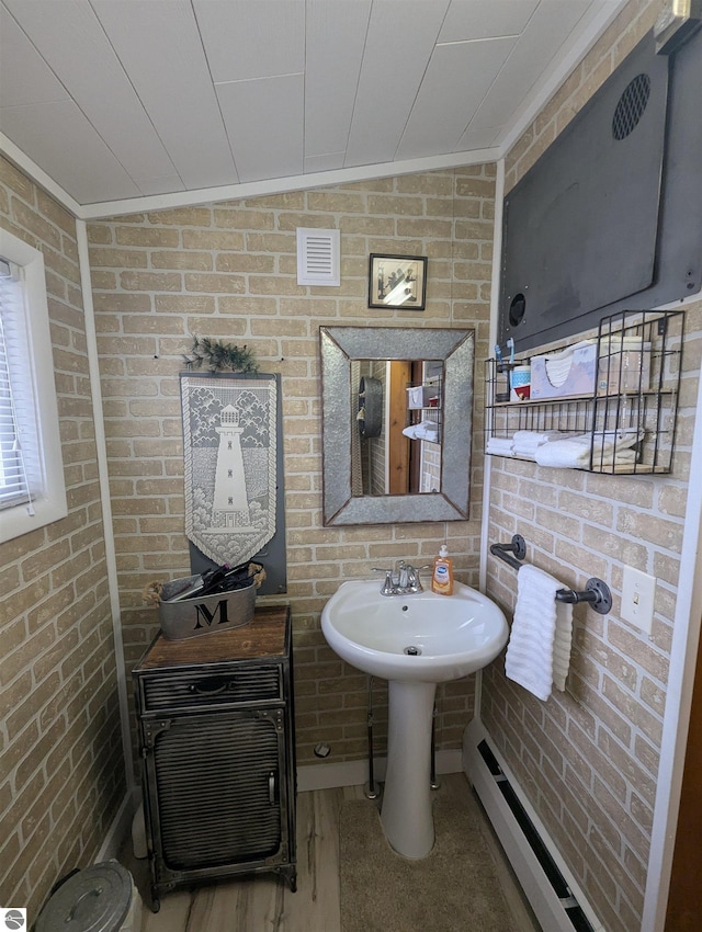 bathroom with a baseboard heating unit, visible vents, brick wall, and a sink