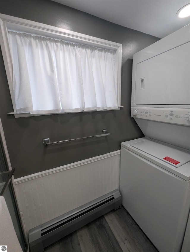 clothes washing area with a baseboard heating unit, a wainscoted wall, laundry area, stacked washer and clothes dryer, and wood finished floors