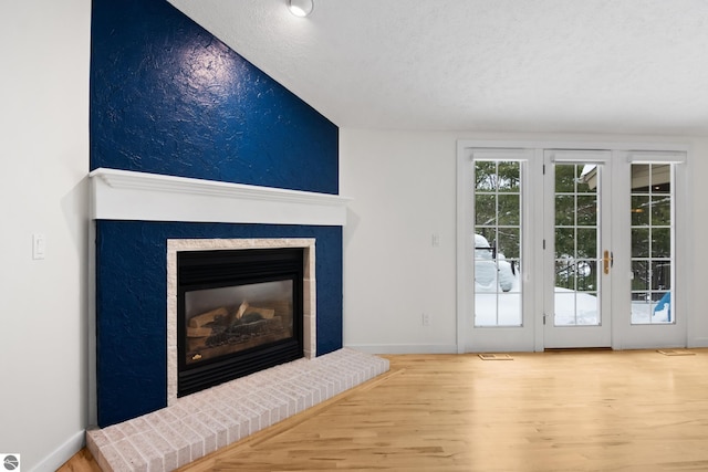 unfurnished living room featuring a glass covered fireplace, wood finished floors, baseboards, and a textured ceiling