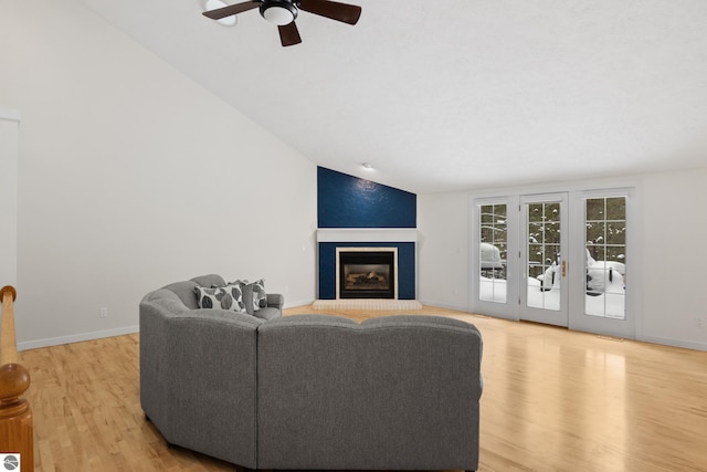 living room featuring baseboards, lofted ceiling, light wood-style flooring, a fireplace, and ceiling fan