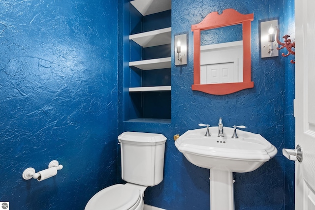 bathroom with toilet, a textured wall, and built in features