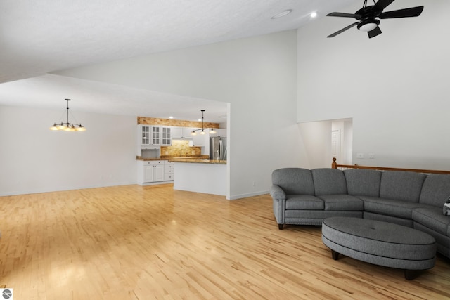 living area with ceiling fan with notable chandelier, high vaulted ceiling, and light wood finished floors