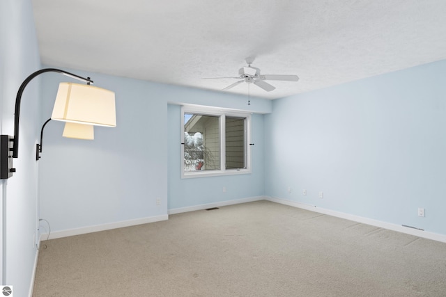 empty room with visible vents, a ceiling fan, a textured ceiling, carpet flooring, and baseboards