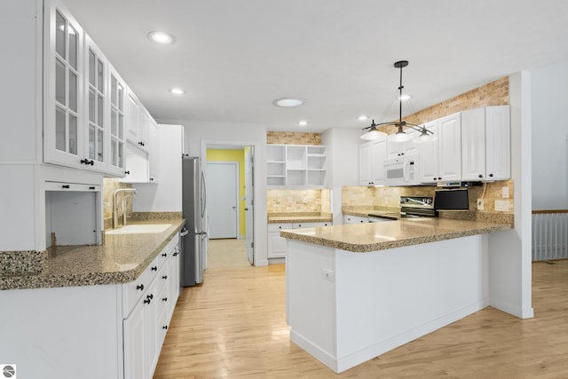 kitchen featuring light wood finished floors, open shelves, a peninsula, a sink, and appliances with stainless steel finishes