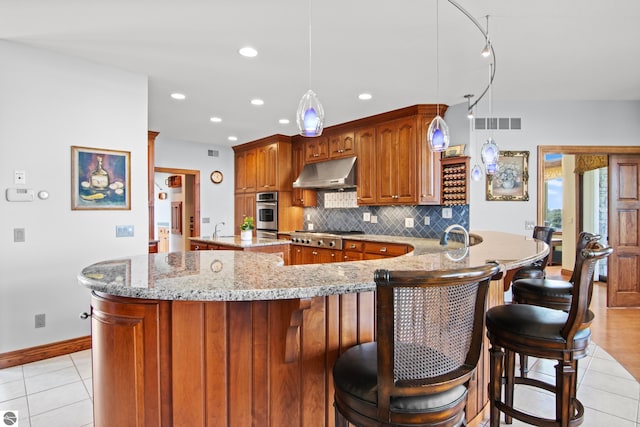 kitchen with visible vents, stainless steel appliances, under cabinet range hood, a kitchen breakfast bar, and tasteful backsplash