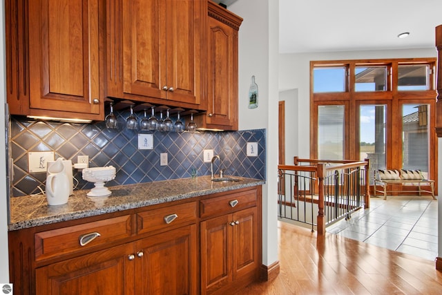 kitchen featuring decorative backsplash, brown cabinets, dark stone counters, and a sink