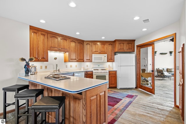 kitchen featuring visible vents, white appliances, a peninsula, and brown cabinets