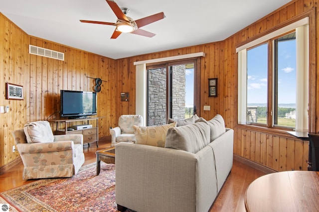 living room with wooden walls, visible vents, ceiling fan, and wood finished floors