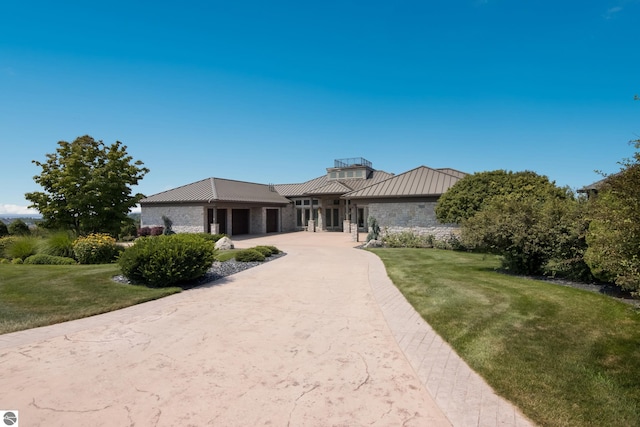 view of front of property with concrete driveway, a front yard, metal roof, stone siding, and a standing seam roof