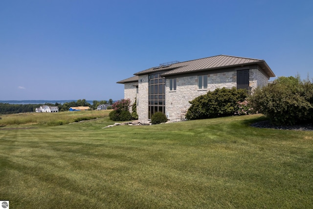 view of home's exterior featuring metal roof, stone siding, a lawn, and a standing seam roof