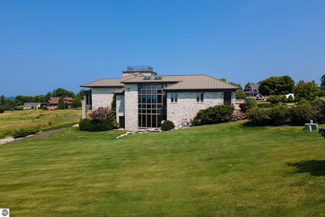 rear view of house featuring a yard, stone siding, metal roof, and a standing seam roof