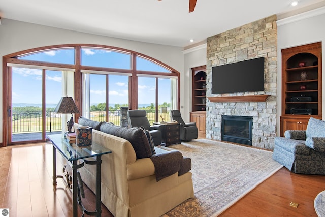 living area featuring built in shelves, ceiling fan, a stone fireplace, recessed lighting, and wood finished floors