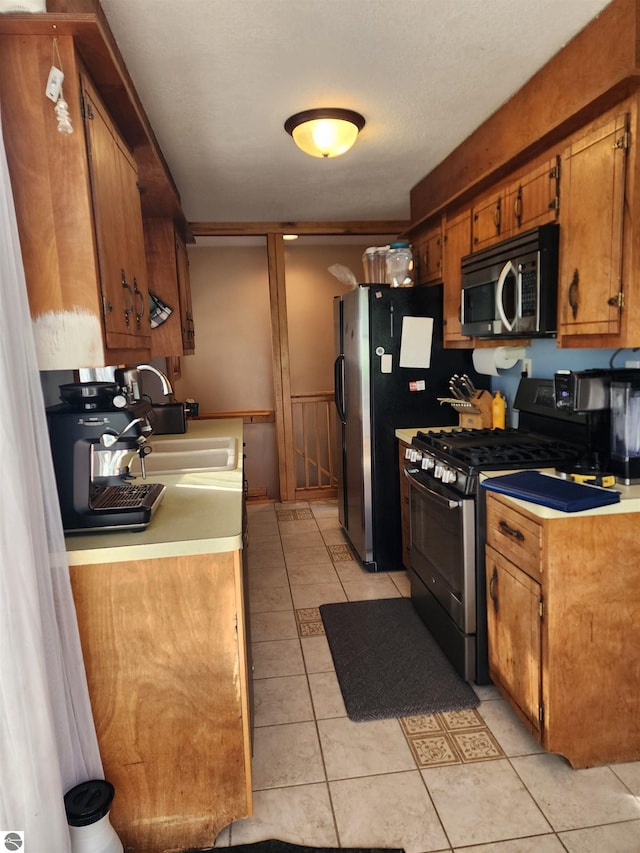 kitchen with a wainscoted wall, a sink, stainless steel appliances, brown cabinetry, and light countertops