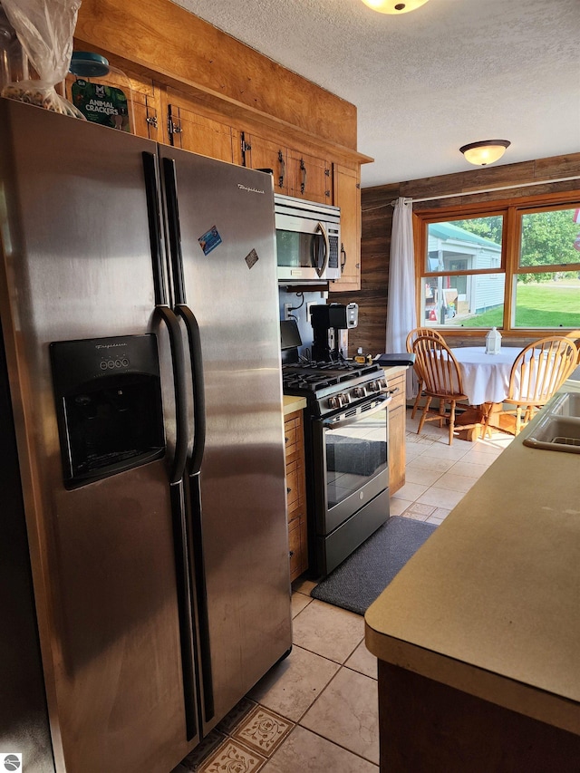 kitchen featuring light tile patterned floors, brown cabinetry, appliances with stainless steel finishes, and a textured ceiling