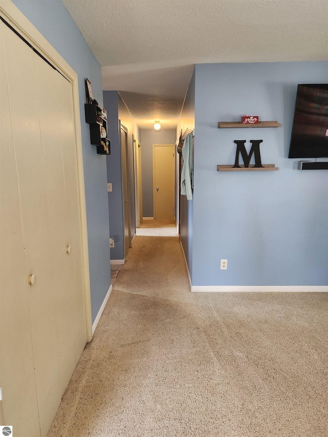 corridor featuring a textured ceiling, baseboards, and carpet floors