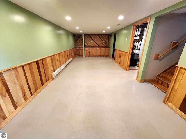 finished basement featuring stairway, wooden walls, a baseboard radiator, recessed lighting, and wainscoting