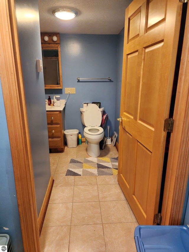 half bath with baseboards, toilet, vanity, and tile patterned flooring