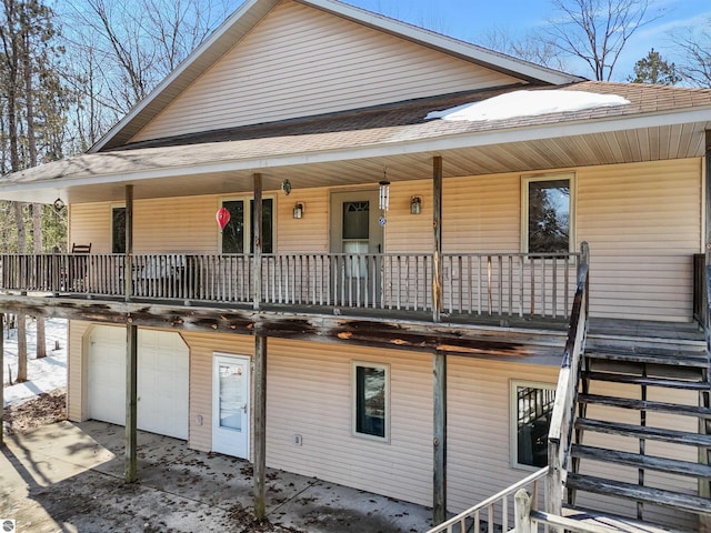 rear view of house featuring stairway, a garage, covered porch, and roof with shingles