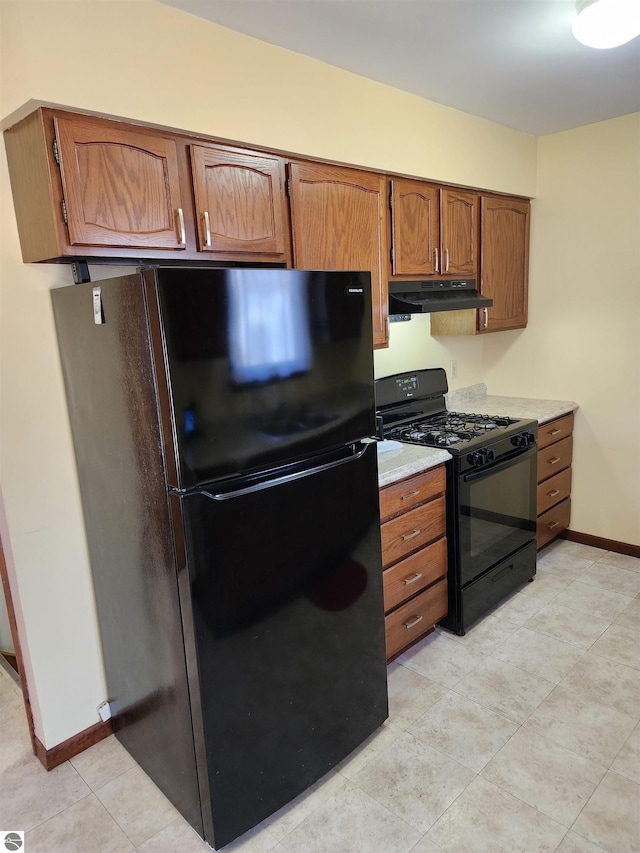 kitchen featuring brown cabinetry, baseboards, black appliances, light countertops, and under cabinet range hood