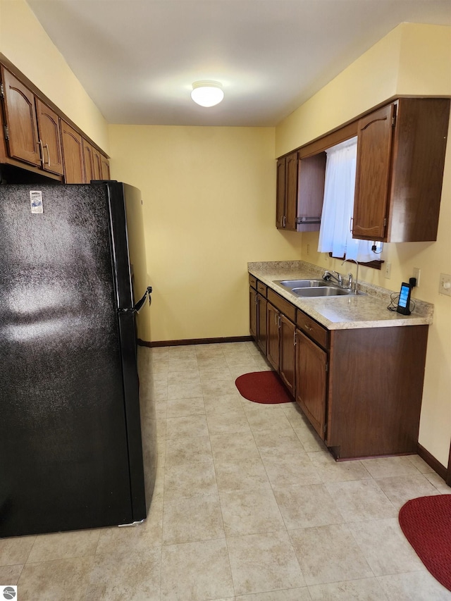 kitchen featuring a sink, freestanding refrigerator, light tile patterned flooring, light countertops, and baseboards