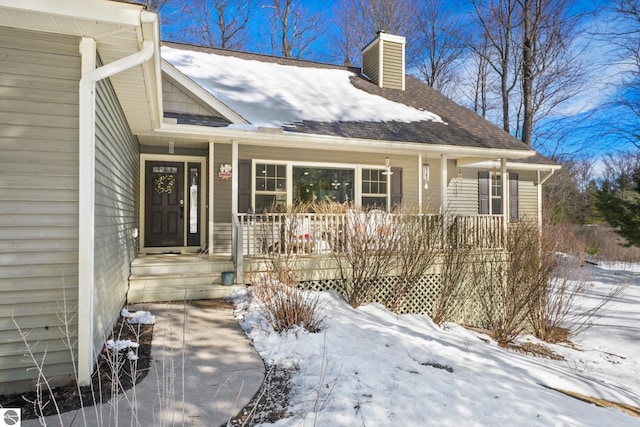 snow covered property entrance with a porch and a chimney