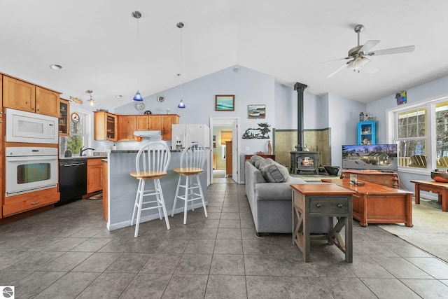 living room featuring ceiling fan, light tile patterned flooring, a wood stove, and vaulted ceiling