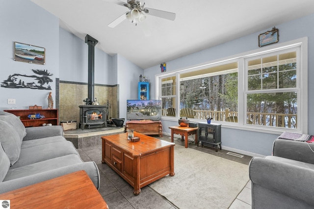 tiled living room with visible vents, lofted ceiling, a ceiling fan, and a wood stove