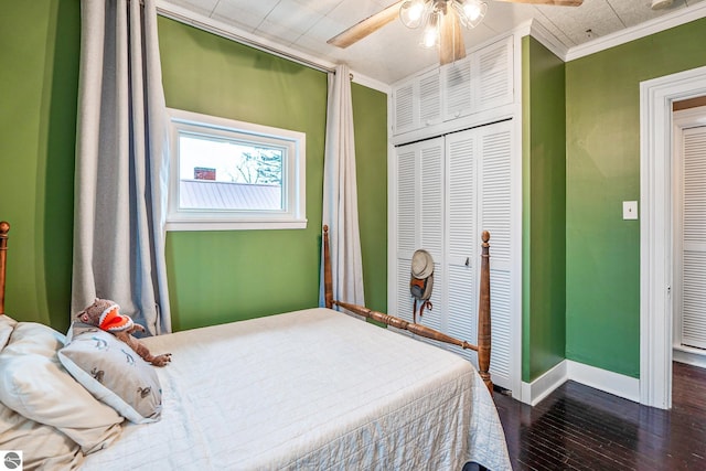 bedroom with baseboards, dark wood finished floors, ceiling fan, a closet, and crown molding