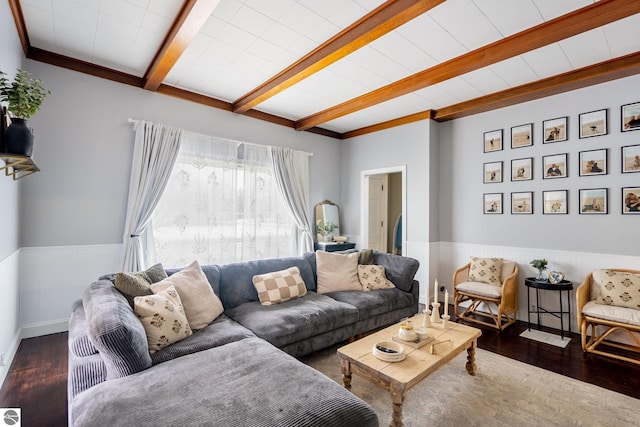 living area featuring beam ceiling, wood finished floors, and a wainscoted wall