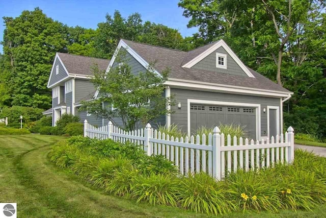 view of front of property featuring a garage, a fenced front yard, and a shingled roof