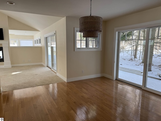 unfurnished dining area featuring a glass covered fireplace, baseboards, lofted ceiling, and hardwood / wood-style floors