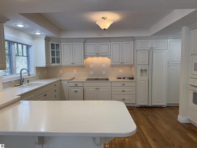 kitchen with dark wood-type flooring, a peninsula, light countertops, glass insert cabinets, and built in appliances