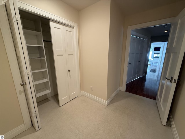 hallway with baseboards and light colored carpet