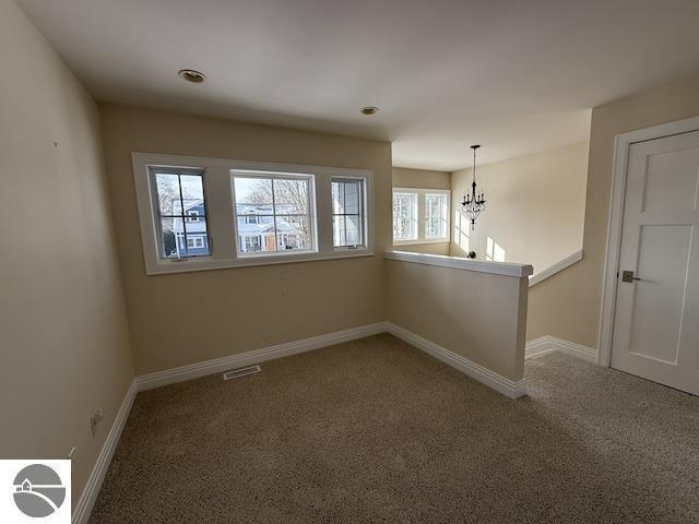 unfurnished room featuring visible vents, baseboards, carpet, and a chandelier