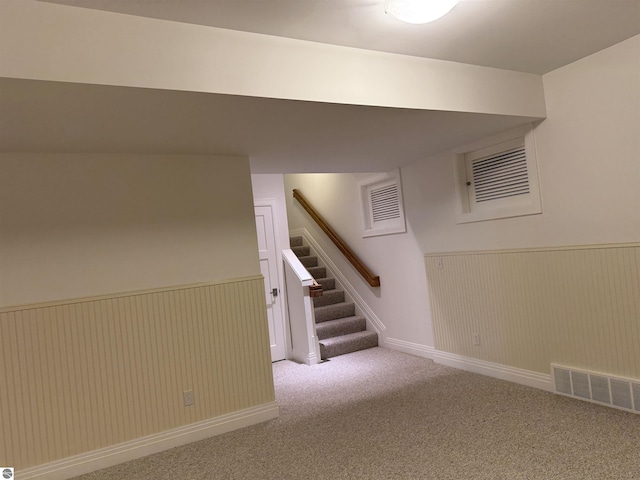 finished basement featuring visible vents, carpet, a wainscoted wall, and stairs