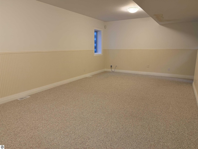 carpeted spare room with visible vents and wainscoting